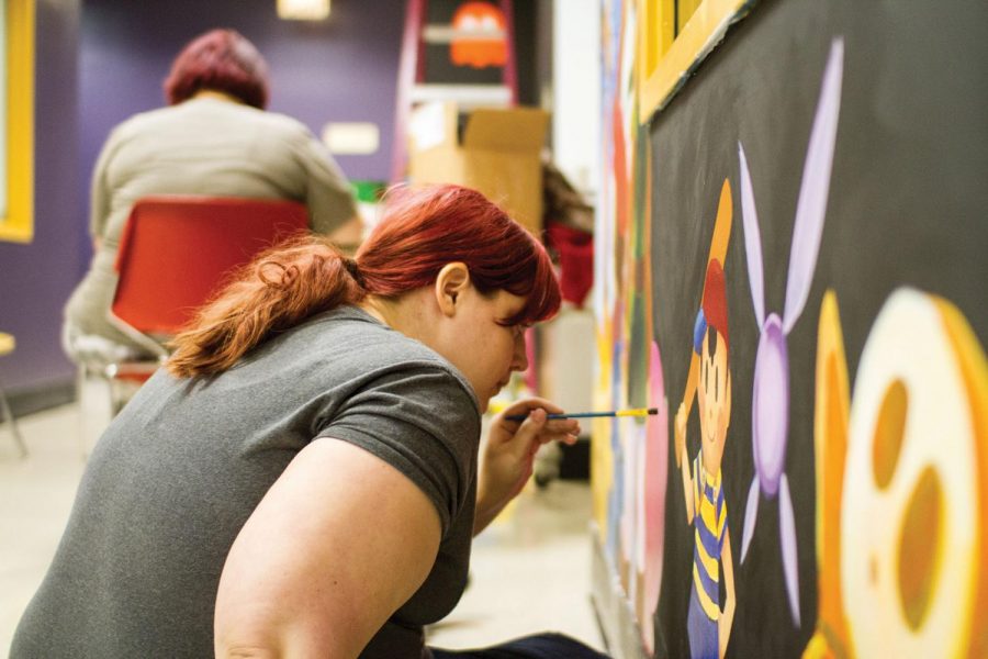 Senior art student Naomi Mongosa decorates the walls outside the Lion’s Den Game Room with artwork. Mongosa began painting the walls June 8.