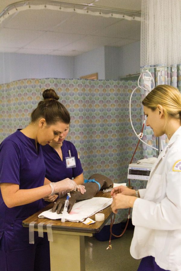 Nursing Student Assistant Shelby Mayhunt (right) walks senior Gabby Kroeger (left) through the procedure for drawing blood.