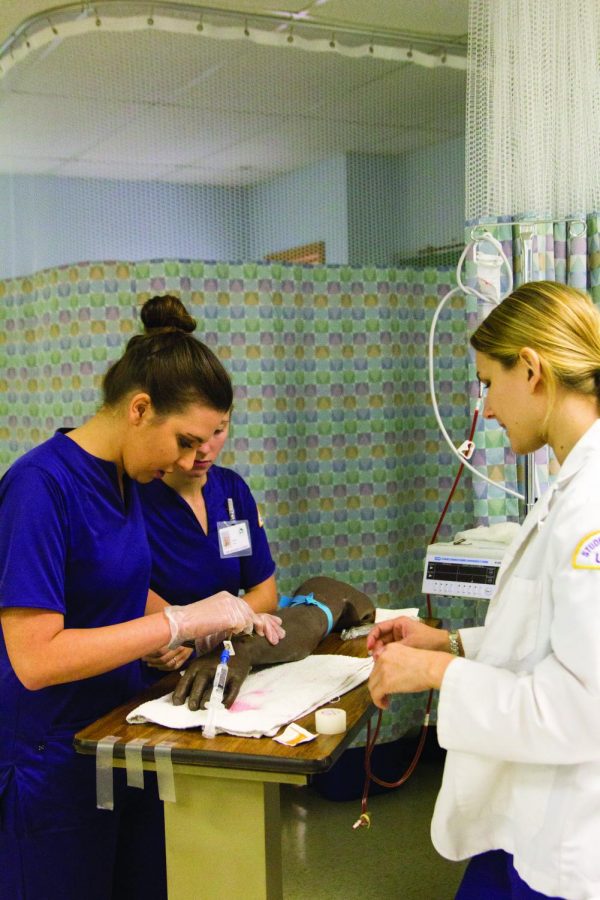 Nursing Student Assistant Shelby Mayhunt (right) walks senior Gabby Kroeger through the procedure for drawing blood. Nursing students will attend a program with a new name this semester.