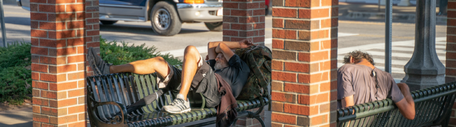 Two homeless men rest on a bench in the heat in downtown Florence. During daylight, these two individuals roam the streets with backpacks and their jackets tied around their waist.